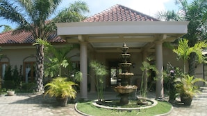 A courtyard with a fountain, palm trees, and a building with a tiled roof. - Villa Pakem (Pakem)