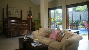 A living room with a sofa, a wooden bench, and a coffee table. There are plants and a window with a view of a garden. - Villa Pakem (Pakem)