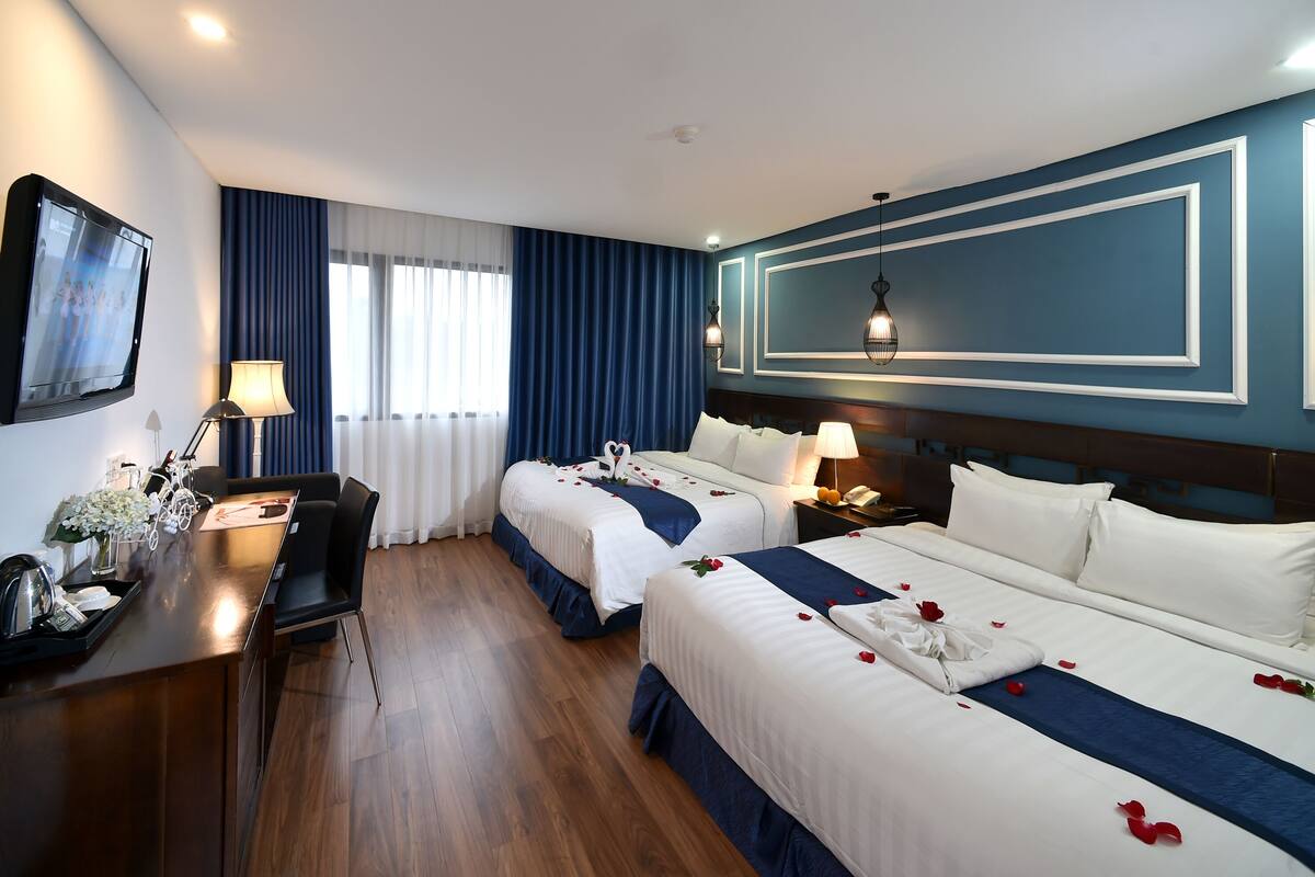 A hotel room with two beds, a desk, a TV, and a dining area.