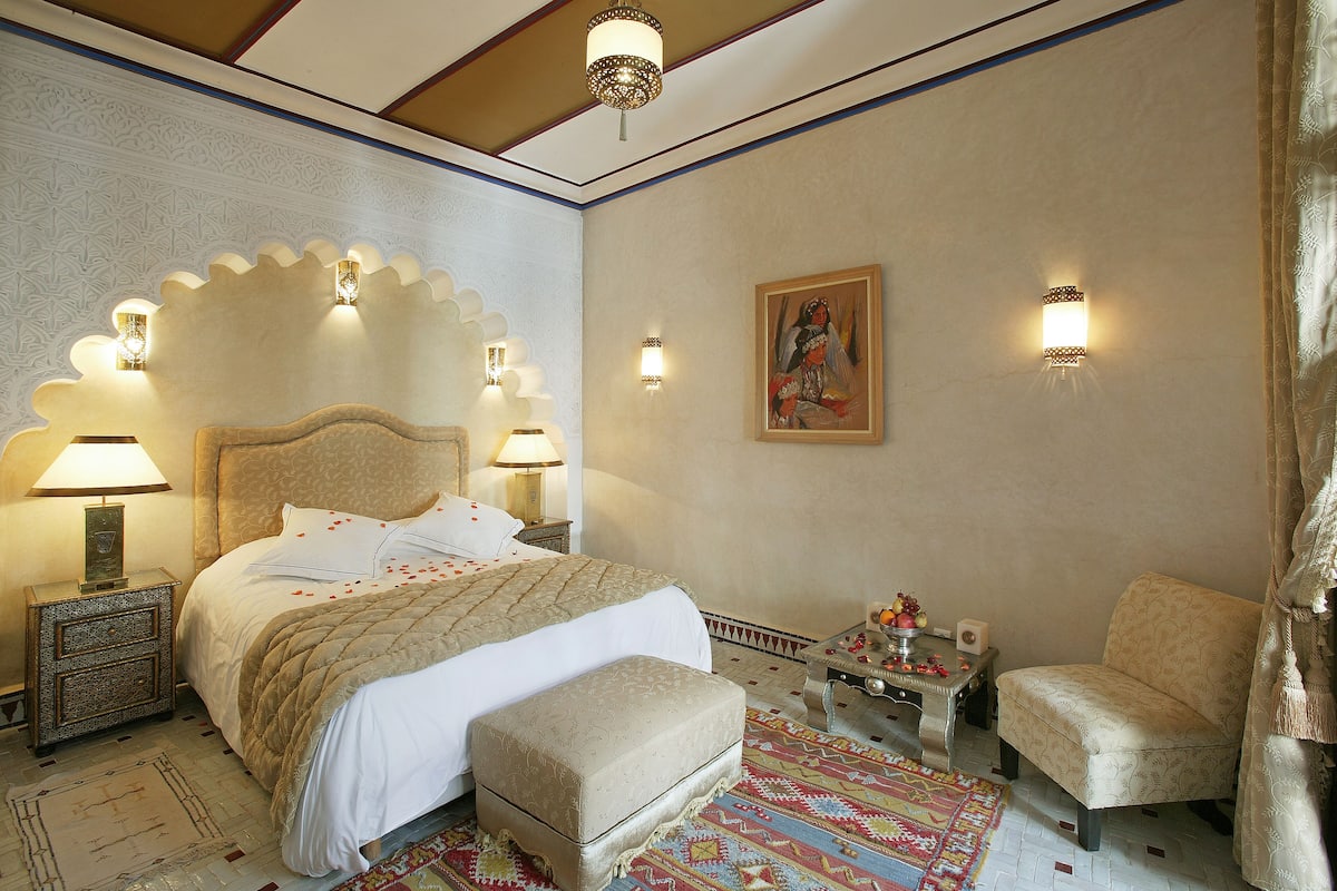 A bedroom with a large bed, a nightstand, a chair, and decorative wall sconces.