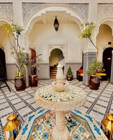 An indoor courtyard with a central fountain, surrounded by arches and potted plants.