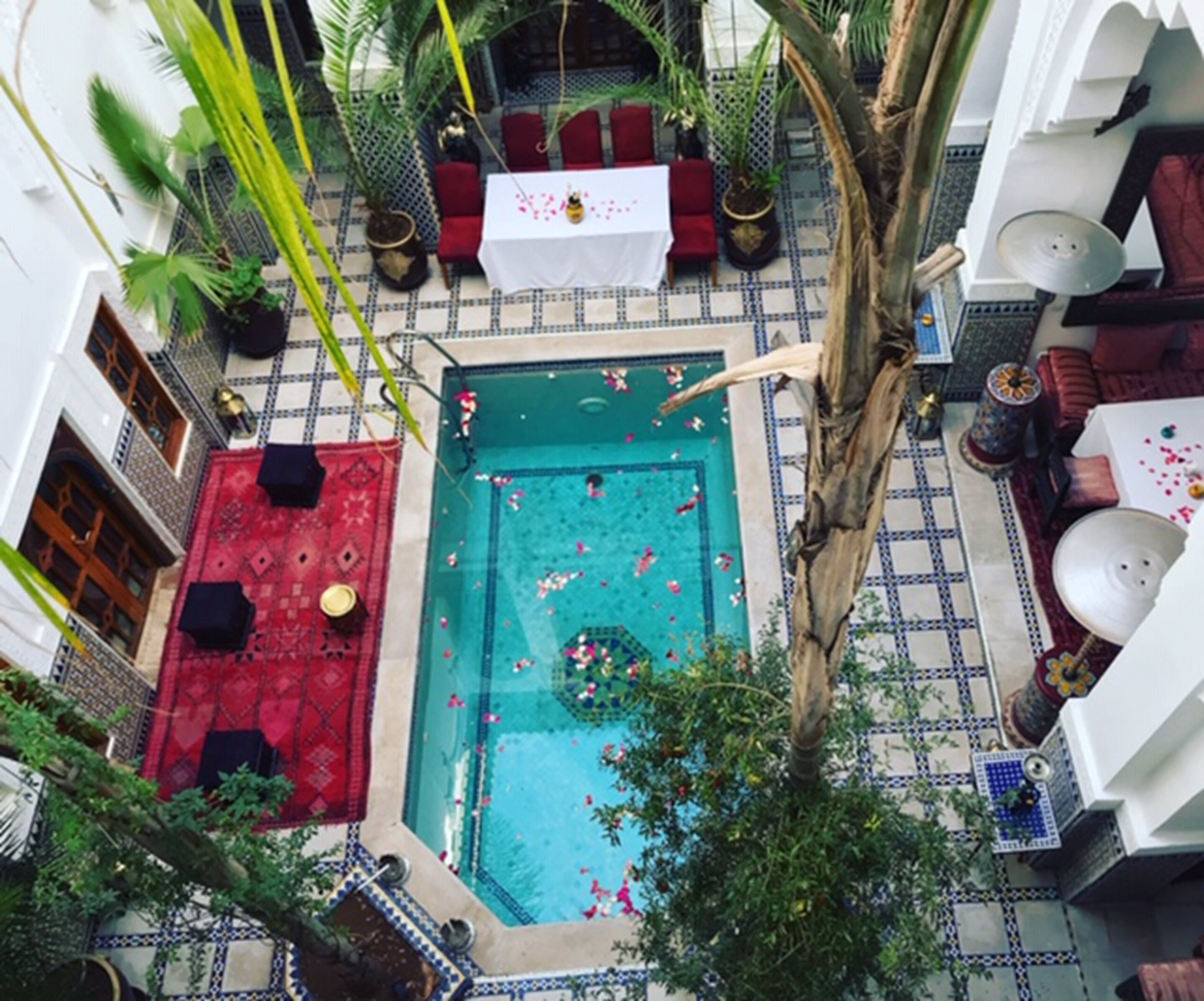 Vue aérienne d’une cour intérieure avec une piscine, un sol à motifs rouges et blancs et une végétation luxuriante tout autour.