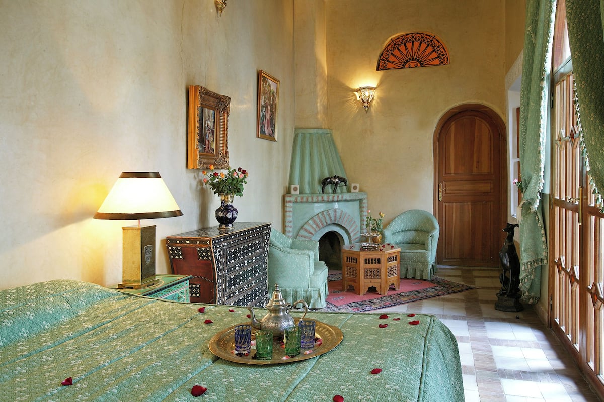 A traditional Moroccan room with a bed, a tea set, a fireplace, and a wooden door.