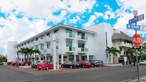 Un hotel moderno con varios balcones, un café y un estacionamiento con varios coches.