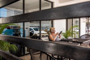 A person seated at a table with a laptop, in front of a window with reflections of parked cars and a building with 'Hotel Pizza' signage. - Hotel Plaza Playa - Near Playa del Carmen Main Beach (Playa del Carmen)