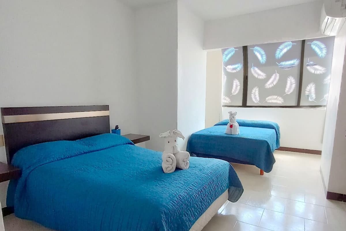 A hotel room with two beds, a nightstand, a towel, and a window with leaf patterns.