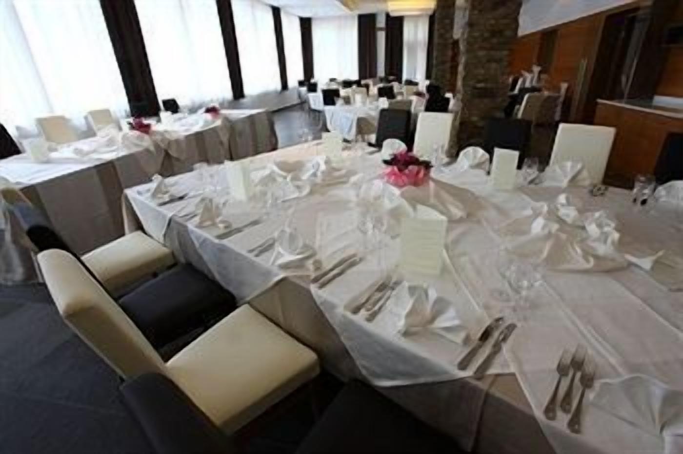 A banquet hall with tables set for a formal event, featuring white tablecloths, neatly arranged cutlery, and chairs.