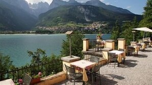 Una terraza con mesas y sillas que da a un lago con montañas al fondo.