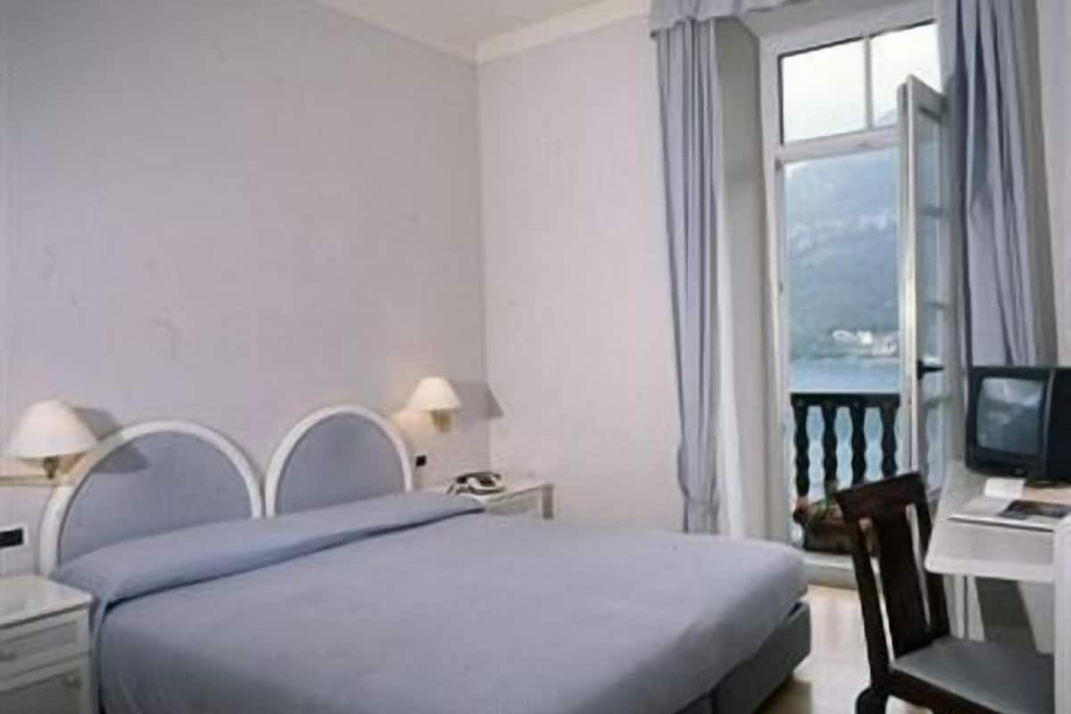 A hotel room with a bed, a desk, a chair, a TV, and a window with curtains.