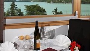 Una mesa dispuesta con una botella de vino, copas y un menú, con vistas a un paisaje montañoso y un lago.