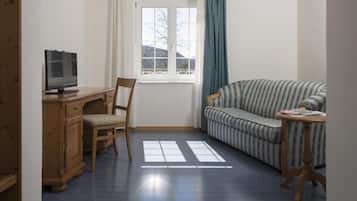 Ein Zimmer mit einem Holztisch, einem Fernseher, einem gestreiften Sofa und einem Fenster mit Vorhängen.