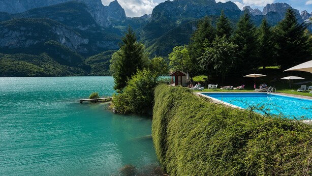 Un lago de montaña con piscina, rodeado de exuberante vegetación y montañas.