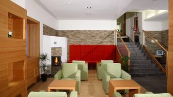 Un vestíbulo moderno con pared de piedra, chimenea, asientos verdes y una escalera.