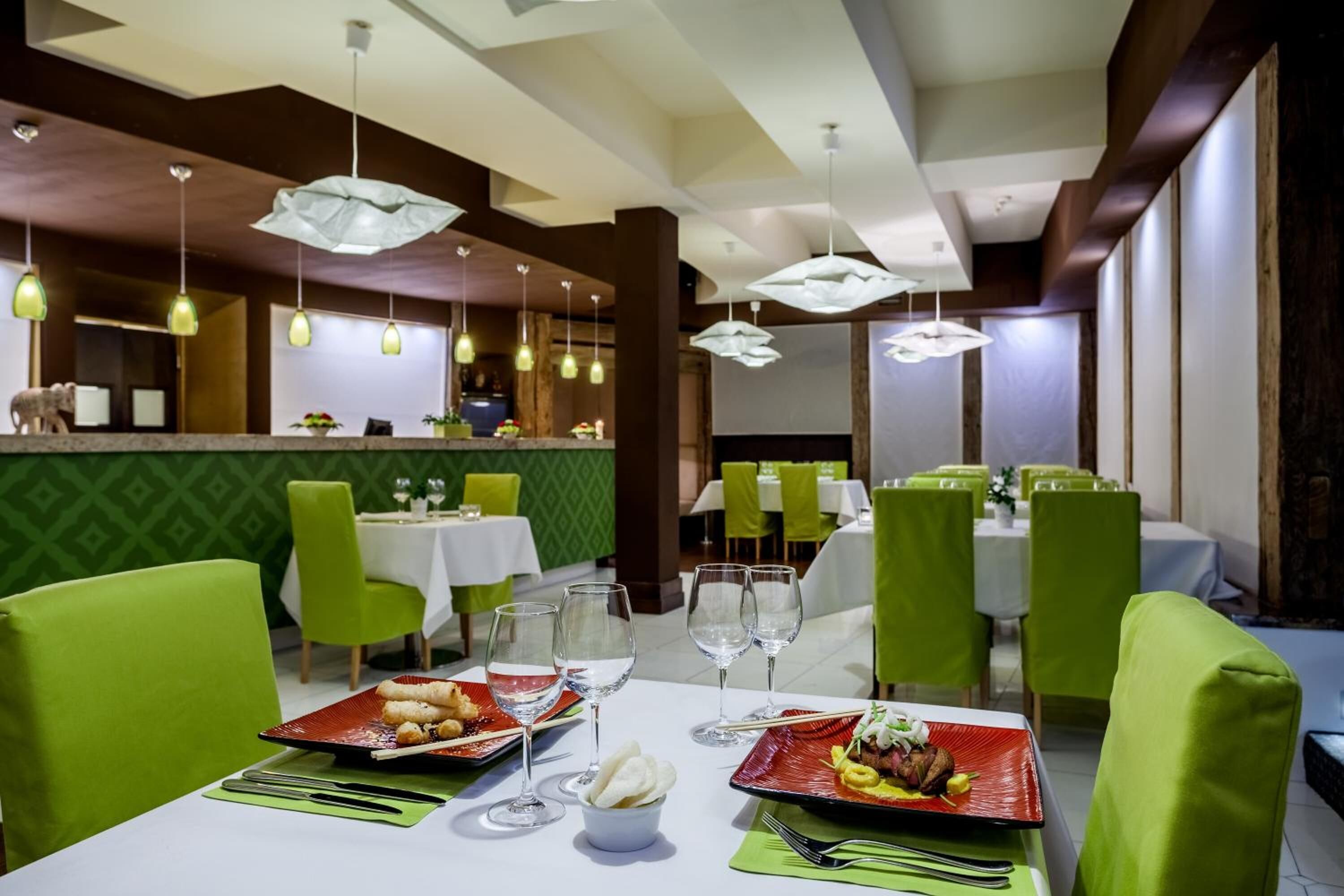 Un restaurante con sillas verdes, mesas blancas y lámparas colgantes.