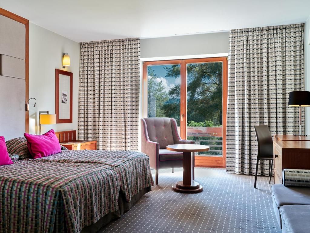 Ein Hotelzimmer mit Bett, Schreibtisch, Stuhl und einem fenster mit Vorhängen.