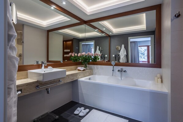 A modern bathroom with a large mirror, two sinks, a bathtub, and a vanity with a towel rack.