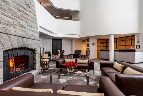 A spacious lobby with a stone fireplace, leather sofas, a glass coffee table, and a reception desk. - Hotel SPA Dr Irena Eris Krynica Zdrój 12+ (Krynica-Zdroj)