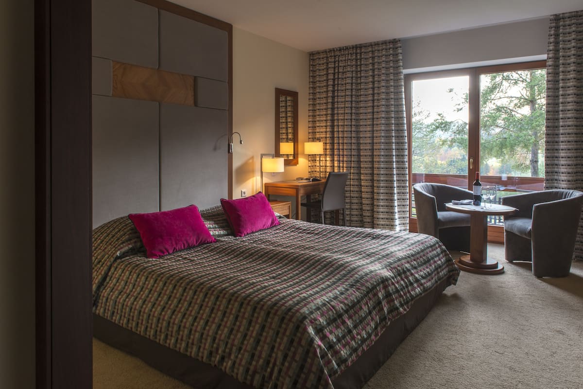 Une chambre d’hôtel avec un grand lit, un bureau, deux chaises et une fenêtre avec des rideaux.
