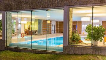 Un hotel moderno con piscina vetrata, facciata in pietra e servizi interni come area reception e bar.