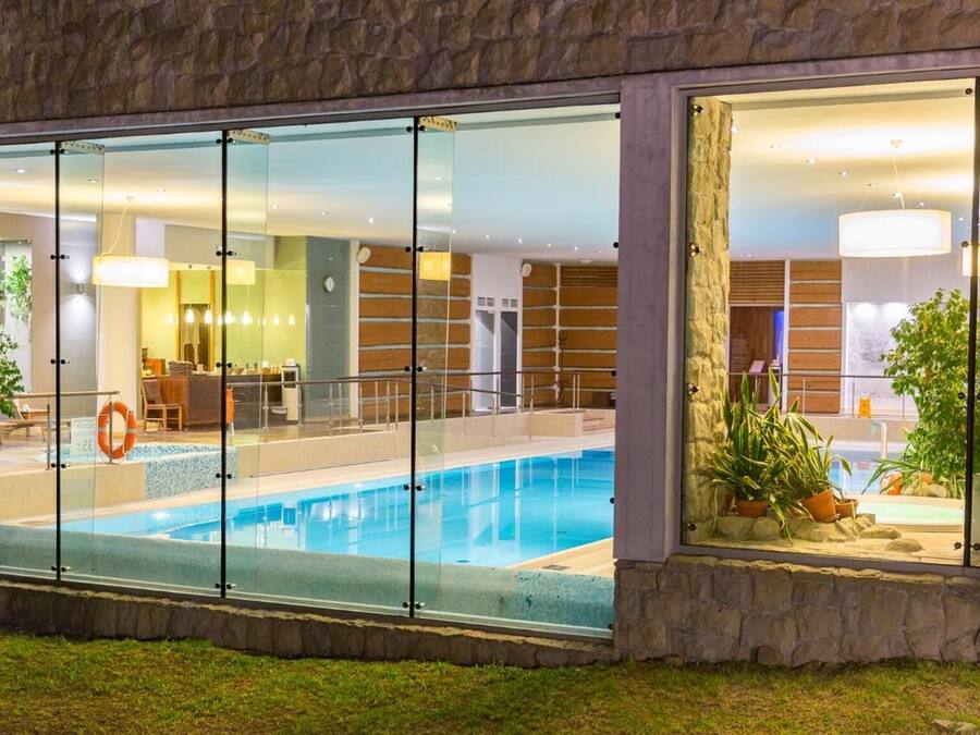 Un hotel moderno con piscina vetrata, facciata in pietra e servizi interni come area reception e bar.