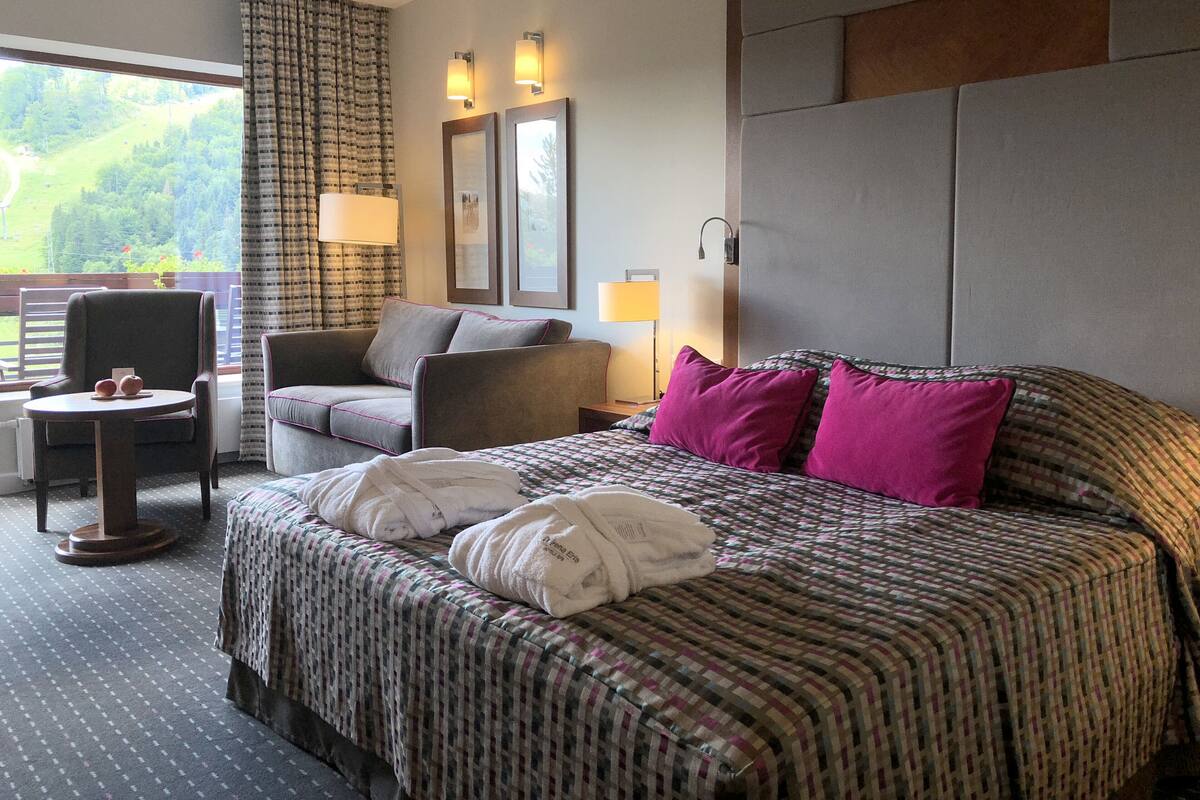 Une chambre d’hôtel avec un grand lit, une chaise, une petite table et une vue sur l’extérieur.