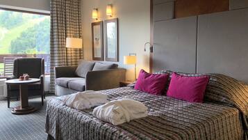 A hotel room with a large bed, a chair, a small table, and a view of the outdoors.