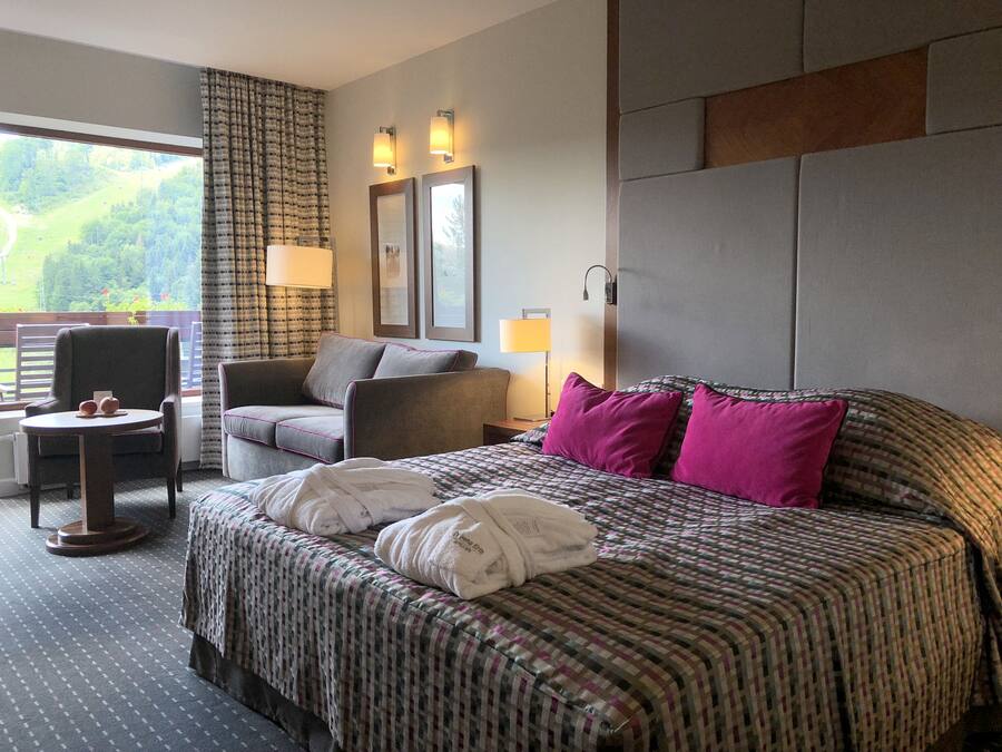 A hotel room with a large bed, a chair, a small table, and a view of the outdoors.