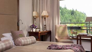 A hotel room with a large bed, a chair, a desk with lamps, and a view of greenery.