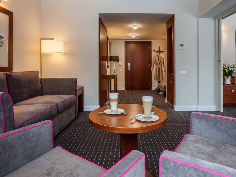 Une chambre d’hôtel avec un canapé, des fauteuils, une table ronde sur laquelle sont posées deux tasses de café, un peignoir accroché à la porte et une lampe fixée au mur.