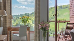 A room with a large window, a wooden desk, a chair, a vase with flowers, and a balcony with chairs. - Hotel SPA Dr Irena Eris Krynica Zdrój 12+ (Krynica-Zdroj)