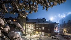 A modern building with large windows and a stone facade, surrounded by snow-covered trees and parked cars. - Hotel SPA Dr Irena Eris Krynica Zdrój 12+ (Krynica-Zdroj)