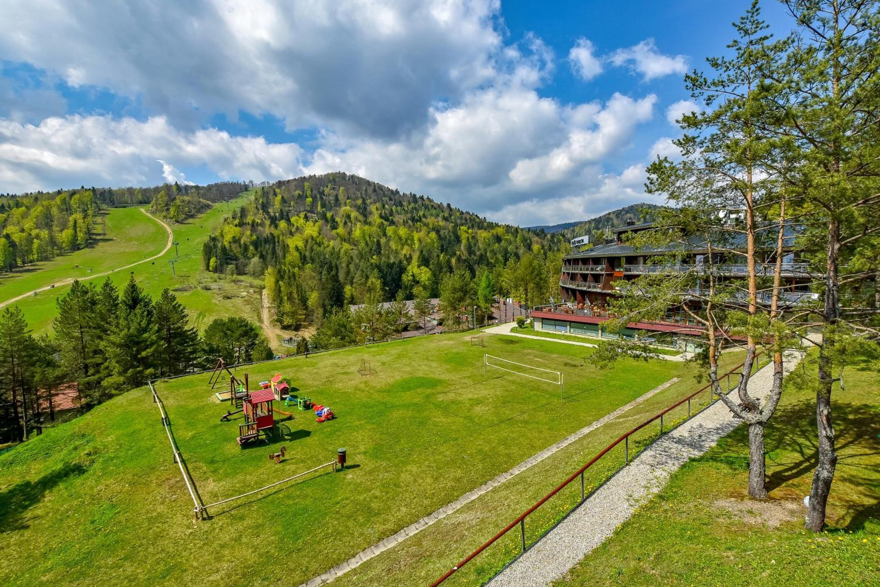 Hotel com vista para um campo verde e uma montanha ao fundo.