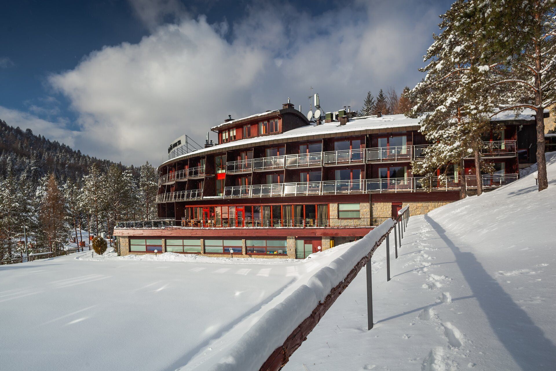 A multi-story hotel with balconies, located on a snowy slope with a mountain backdrop.