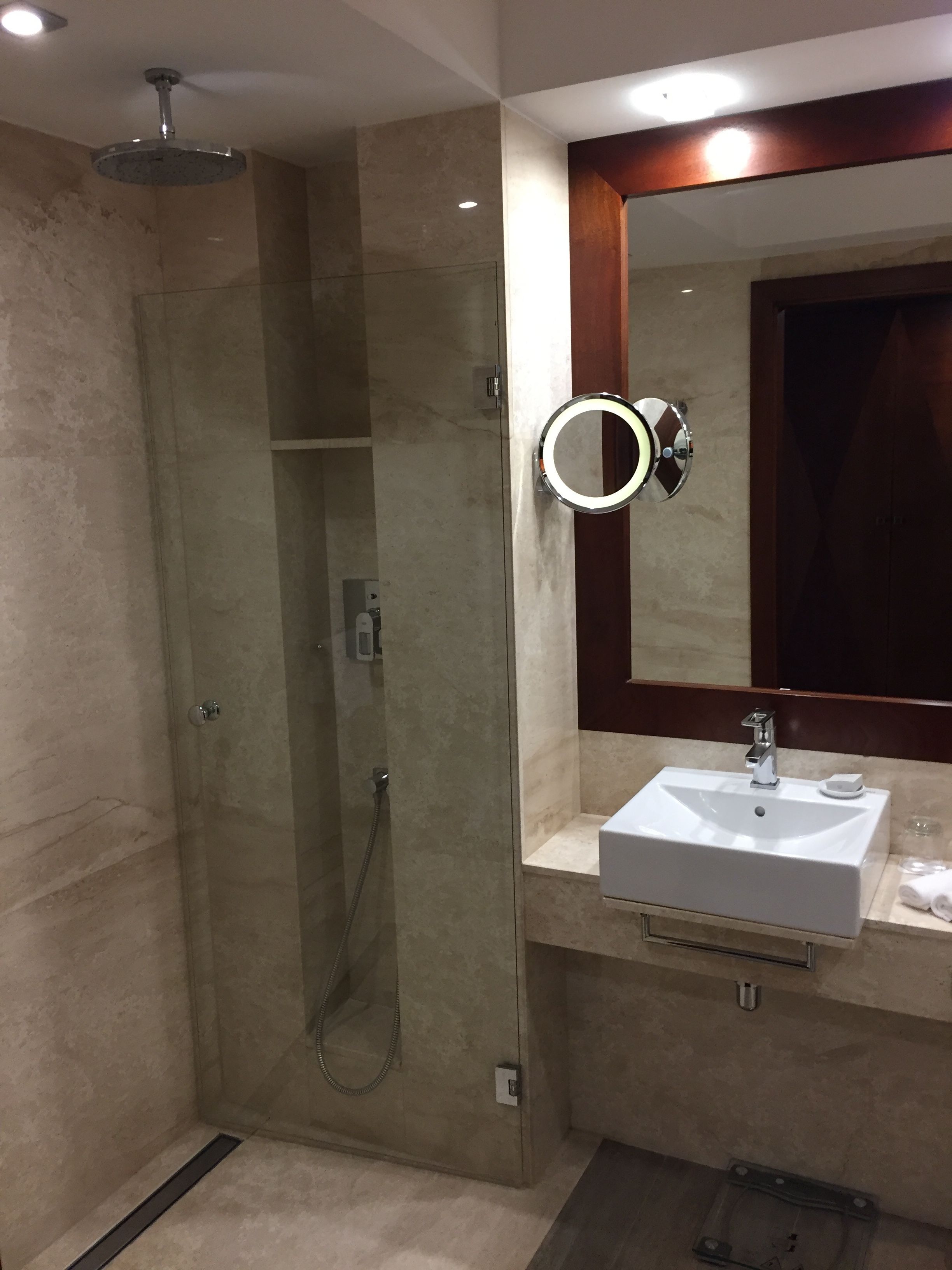 Un baño moderno con ducha envuelta en vidrio, tocador con lavamanos y espejo con luz de aro.