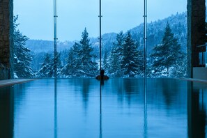 A large indoor swimming pool with a view of snow-covered trees and mountains.