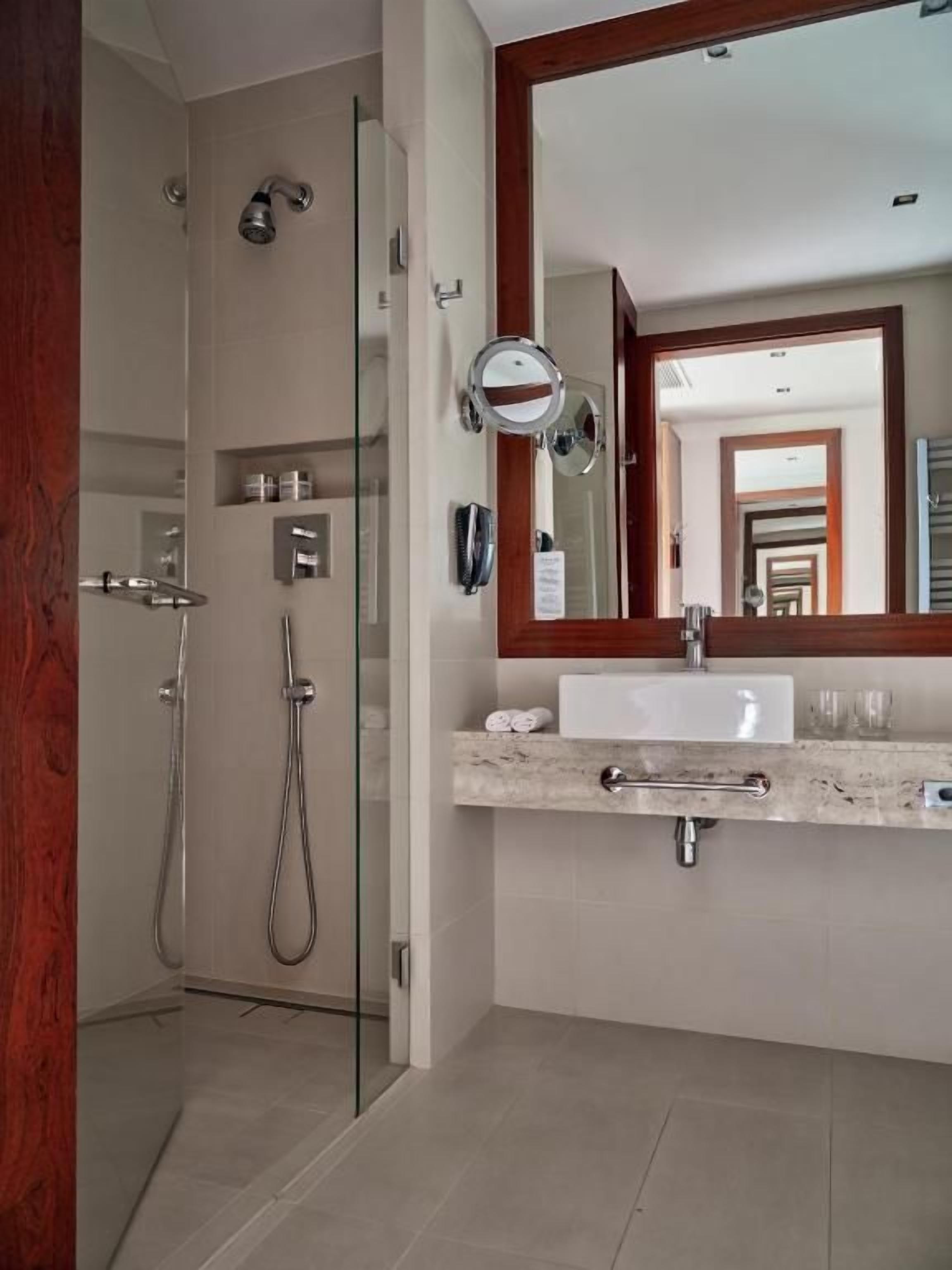 Une salle de bain moderne avec une douche à parois de verre, un grand miroir et un plan de toilette en marbre.