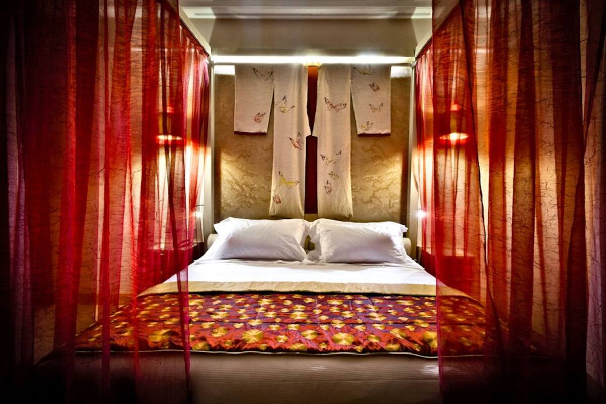 A bed with white linens, red curtains, and a patterned bedspread.
