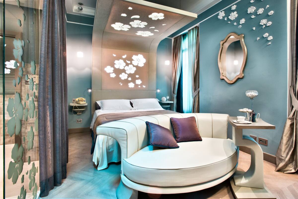 A modern bedroom with a curved bed, a bedside table, a mirror, and a decorative ceiling light.