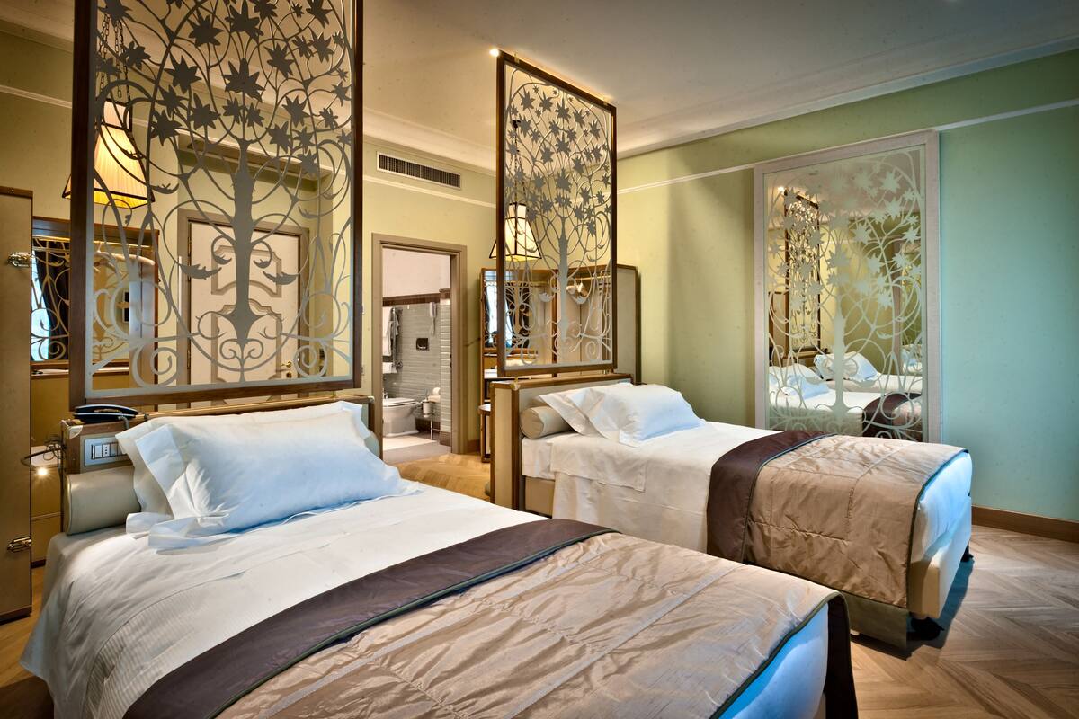 A hotel room with two beds, a wooden floor, and decorative screens with leaf patterns.