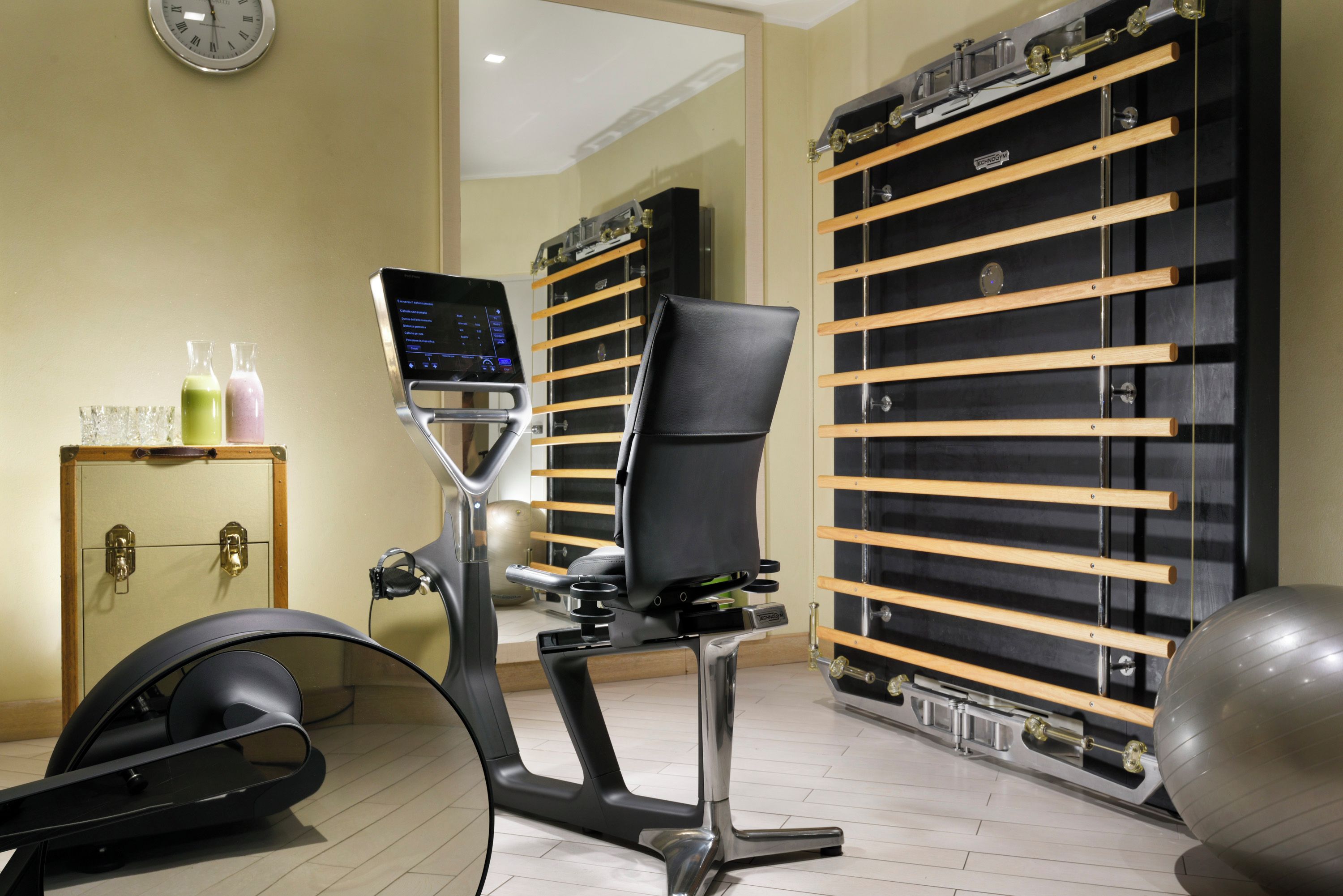 A modern gym with exercise equipment, a digital display, and a mirrored wall.