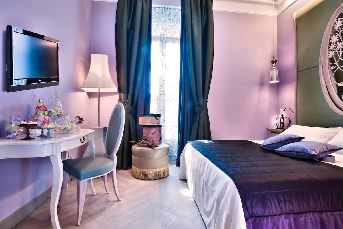 A hotel room with a bed, a desk with a chair, a TV, and a window with curtains.