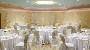 Een feestzaal met ronde tafels, witte tafelkleden en stoelen met witte hoesjes.