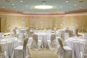 A banquet hall with round tables, white tablecloths, and chairs with white covers.