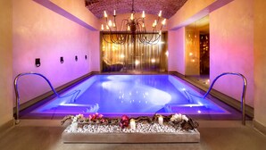 A spa room with a large heated pool, a chandelier, and a decorative arrangement of flowers and candles. - Château Monfort (Milan)
