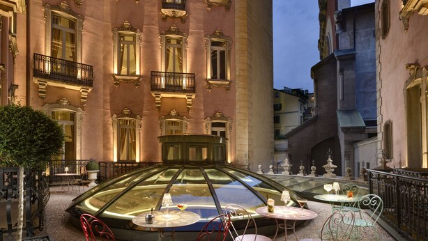 A courtyard with a glass-enclosed car, outdoor seating, and ornate balconies. - Château Monfort (Milan)