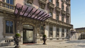 The exterior of the Château Montfort hotel with ornate architecture, a grand entrance, and two large vases with greenery. - Château Monfort (Milan)