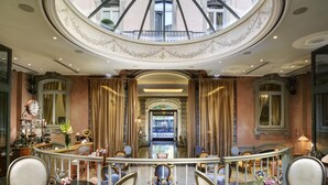 A luxurious hotel lobby with a grand staircase, elegant seating, and a large skylight. - Château Monfort (Milan)