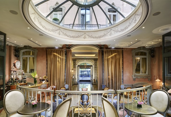 A luxurious hotel lobby with a grand staircase, elegant seating, and a large skylight.