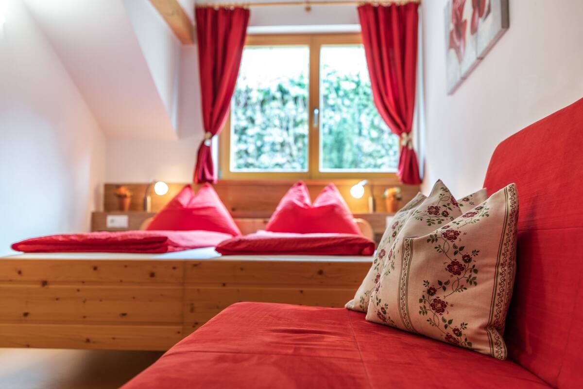 A cozy bedroom with a wooden bed, red bedding, and a window with red curtains.