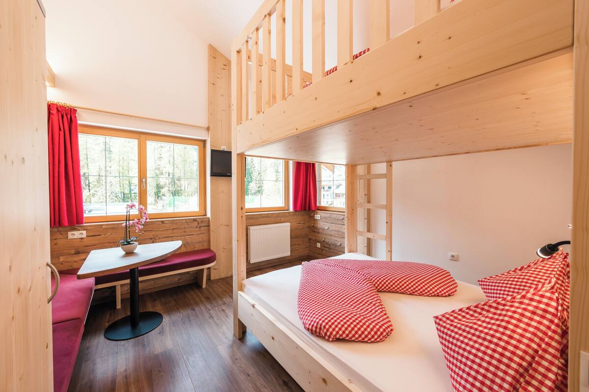 A cabin with a bunk bed, a small table with a chair, and a bench.